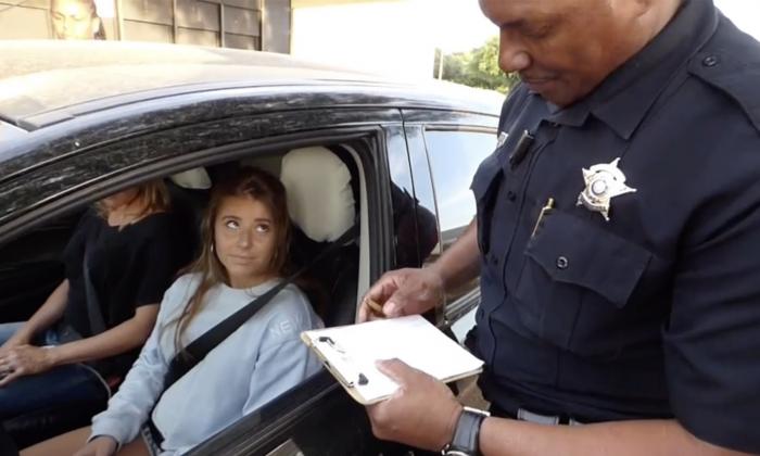 Officer reviewing documents on a clipboard while nervous teenagers in car look on.